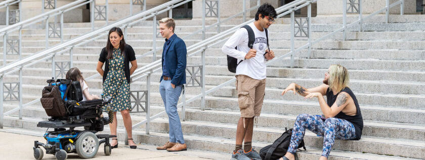 A group of people talk on the steps of a university building