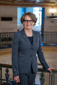 Provost McCauley poses in a blue suit by bannister in the Ruthven bldg