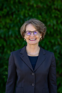 Provost Laurie McCauley Headshot in blue suit in front of green plant wall