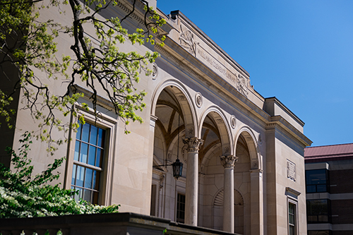 The stone architecture of the Clements Library on a bright spring day under a clear blue sky.