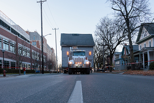 The Raoul Wallenberg House moves slowly down the road on a trailer attached to a white semi truck as it is transferred from its original location on Madison Street to its new home on Division.